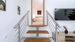 Eine moderne Treppe mit Metallgeländern, Holzbodenstufen und einem Marmorboden, die zu einem Schlafzimmer mit Bett, Nachttisch und einem an der Wand befestigten Flachbildfernseher führt.