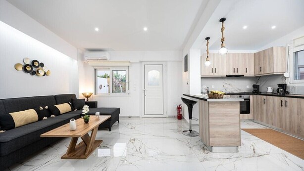 Eine moderne Küche mit Holzschränken, einer zentralen Kochinsel und einem Essbereich mit einer schwarzen Couch und einem Holztisch.