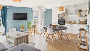 Ein modernes Wohnzimmer mit einer Couch, einem Couchtisch und einem Essbereich mit Stühlen. Es gibt eine Küche mit Schränken, einer Mikrowelle und einer Kaffeemaschine.