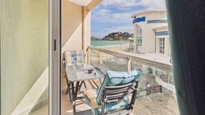 Ein Balkon mit Tisch und Stühlen, Blick auf das Meer und ein Gebäude mit einem Schild.