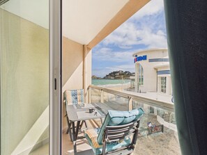 Ein Balkon mit Tisch und Stühlen, Blick auf das Meer und ein Gebäude mit einem Schild.