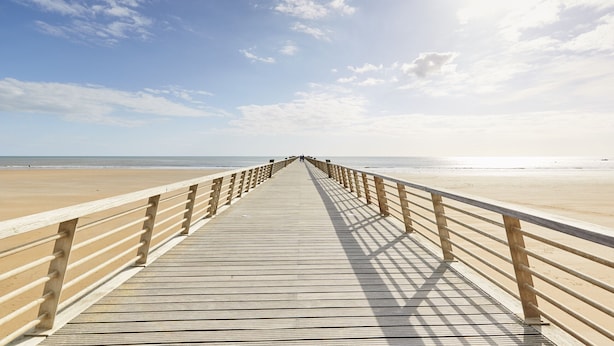 Una passerella di legno che conduce a una spiaggia sotto un cielo sereno.