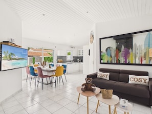 Ein modernes Wohnzimmer mit einer Couch, einem Fernseher und einem Essbereich mit Stühlen und einem Tisch.