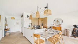 Eine moderne Küche mit weißen Schränken, einer zentralen Kochinsel und einem Essbereich mit Holztischen und -stühlen.