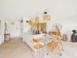 Eine moderne Küche mit weißen Schränken, einer zentralen Kochinsel und einem Essbereich mit Holztischen und -stühlen.