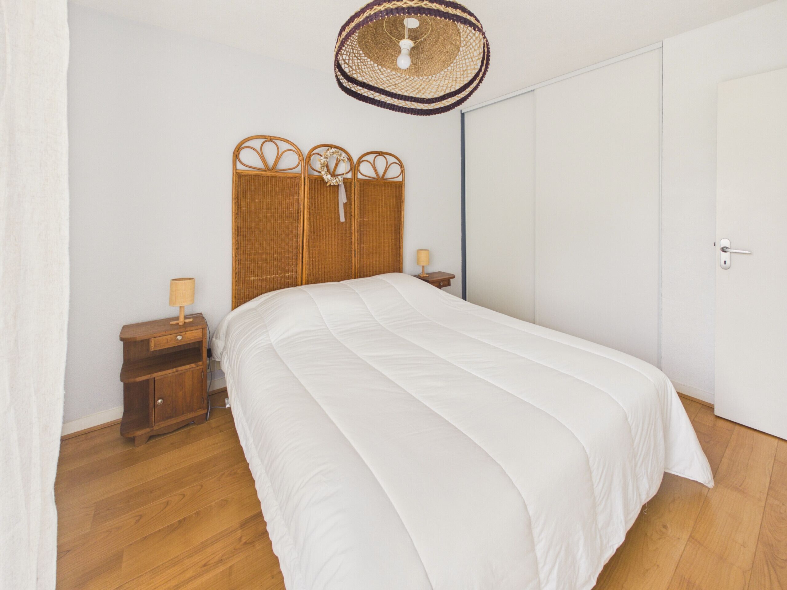A bedroom with a bed, a nightstand, a lamp, a woven headboard, and a door.