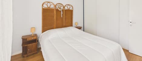 A bedroom with a bed, a nightstand, a lamp, a woven headboard, and a door.