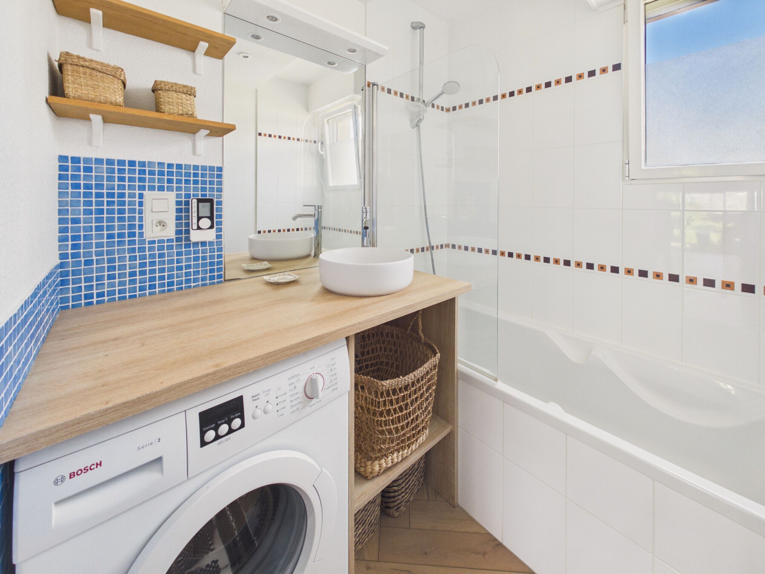 Ein Badezimmer mit Waschmaschine, Waschbecken, Dusche und Spiegel.