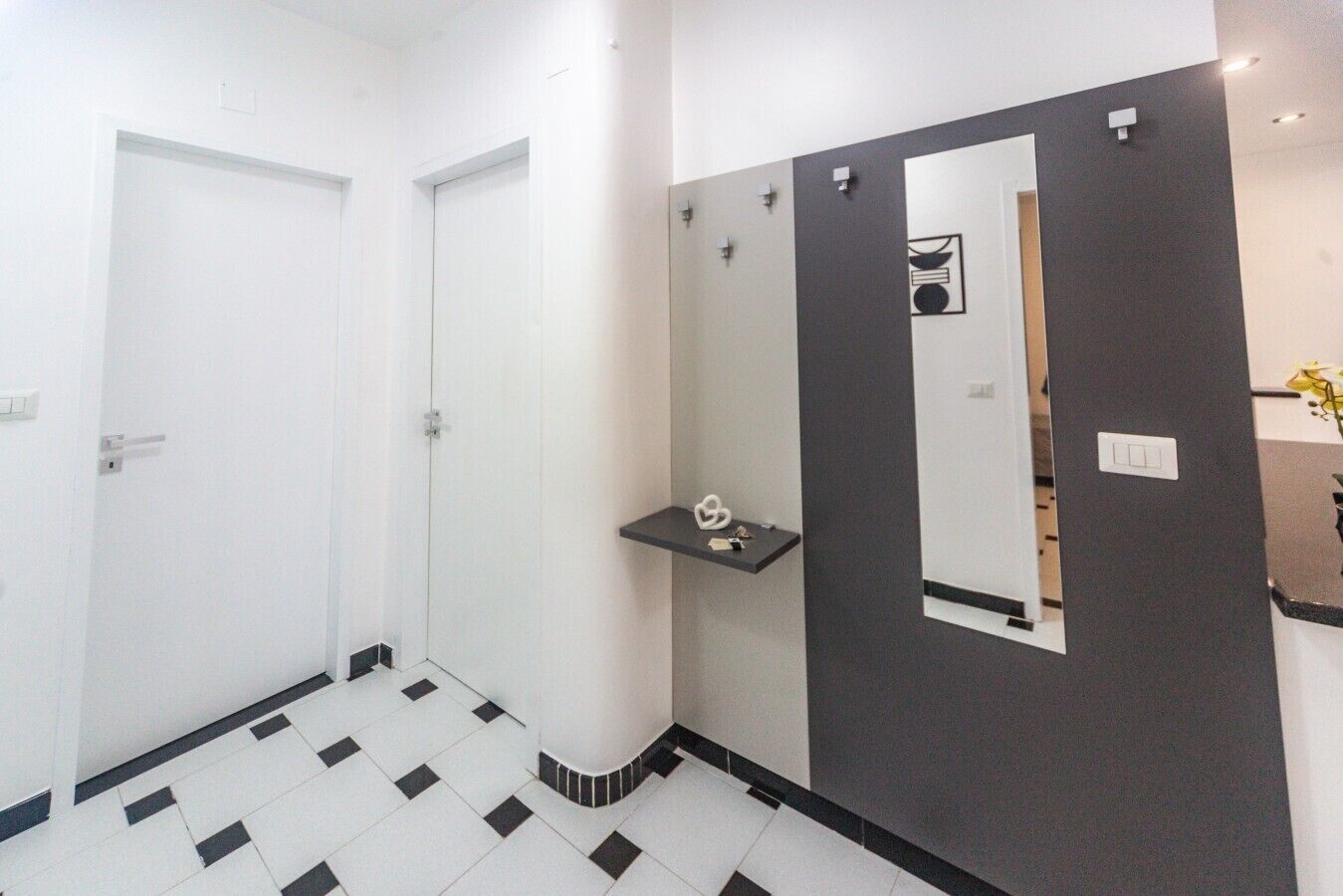 Ein Zimmer mit zwei weißen Türen, einem Spiegel, einer kleinen Ablagefläche und einem gefliesten Boden.