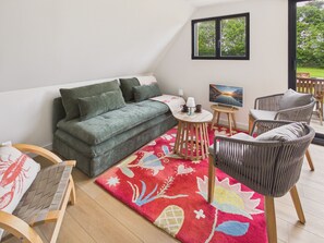 A modern living room with a green sofa, a wooden coffee table, wicker chairs, and a colorful rug.