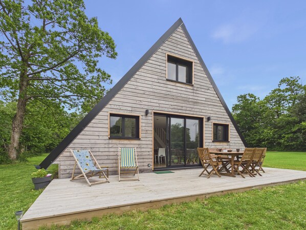 Une maison en bois de forme triangulaire, dotĂ©e dâune terrasse, de coins salon extĂ©rieurs et dâune grande porte-fenĂȘtre coulissante.