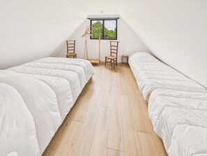 A room with two beds, a window, and a wooden floor.