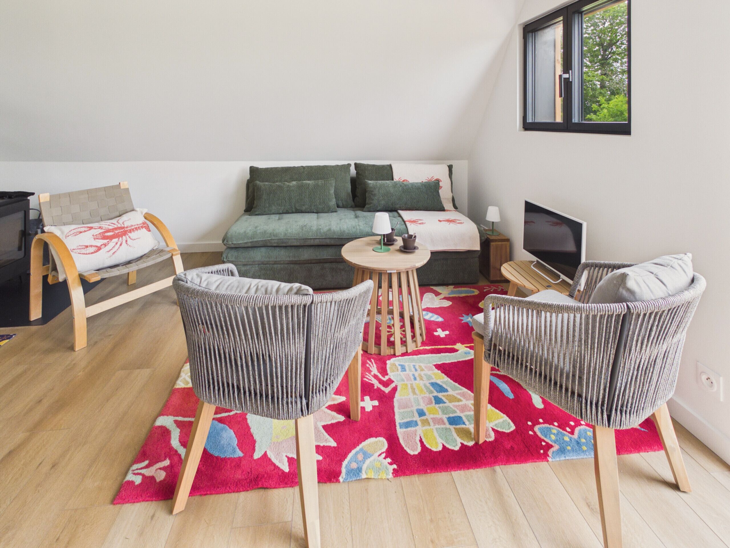 A room with a bed, a TV, two chairs, a small table, and a colorful rug.