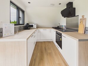 Une cuisine moderne avec des meubles blancs, un four Ă micro-ondes, une cuisiniĂšre et une grande fenĂȘtre.