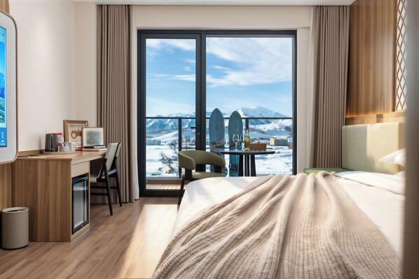 Habitación de hotel con cama, escritorio, silla, una mesita y vistas a montañas a través de amplias ventanas.