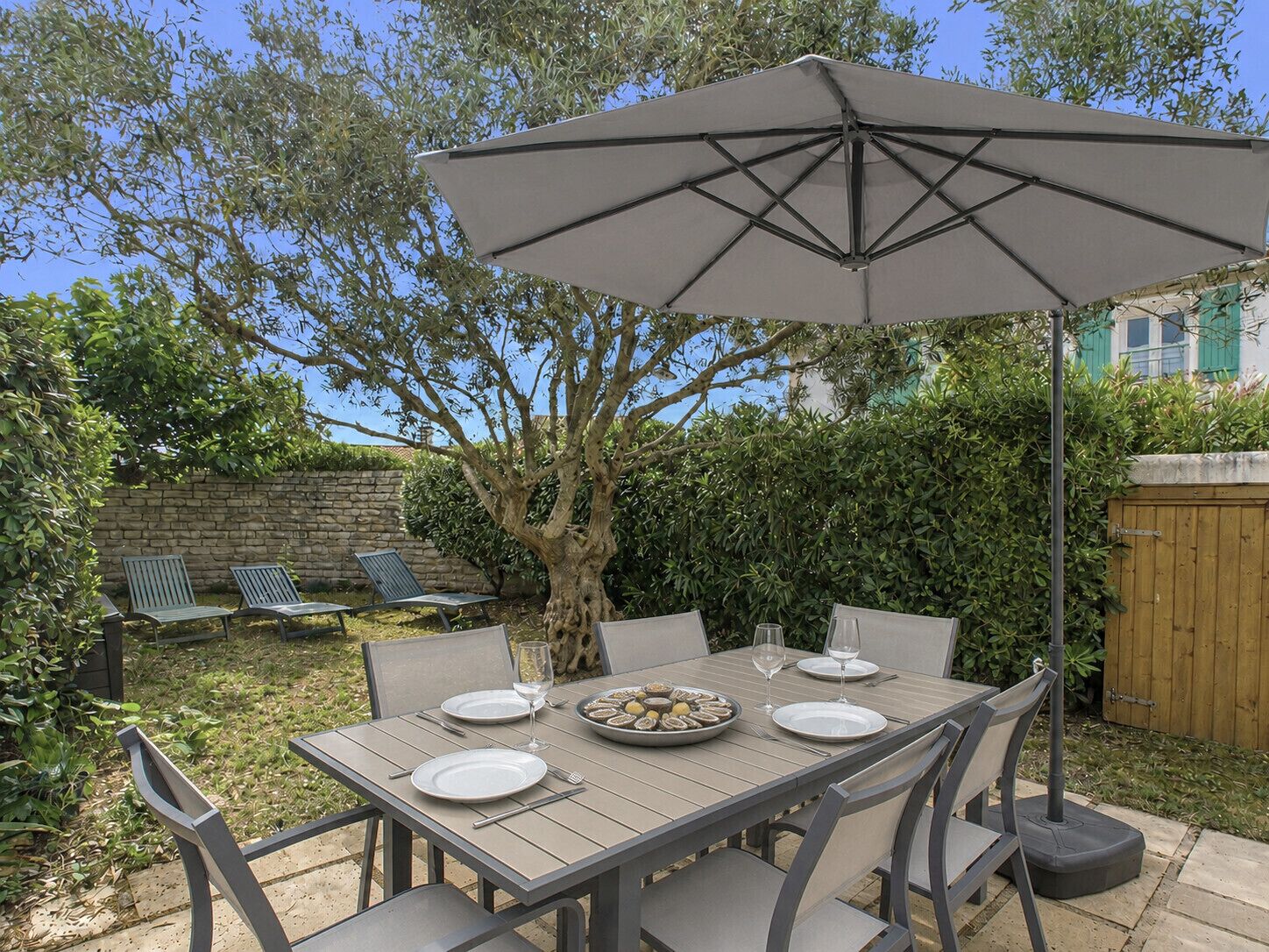 A patio with a table set for four, surrounded by chairs, under a large umbrella.