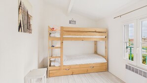 Una cama litera en una habitación con paredes blancas, una mesita pequeña y una ventana con vistas.