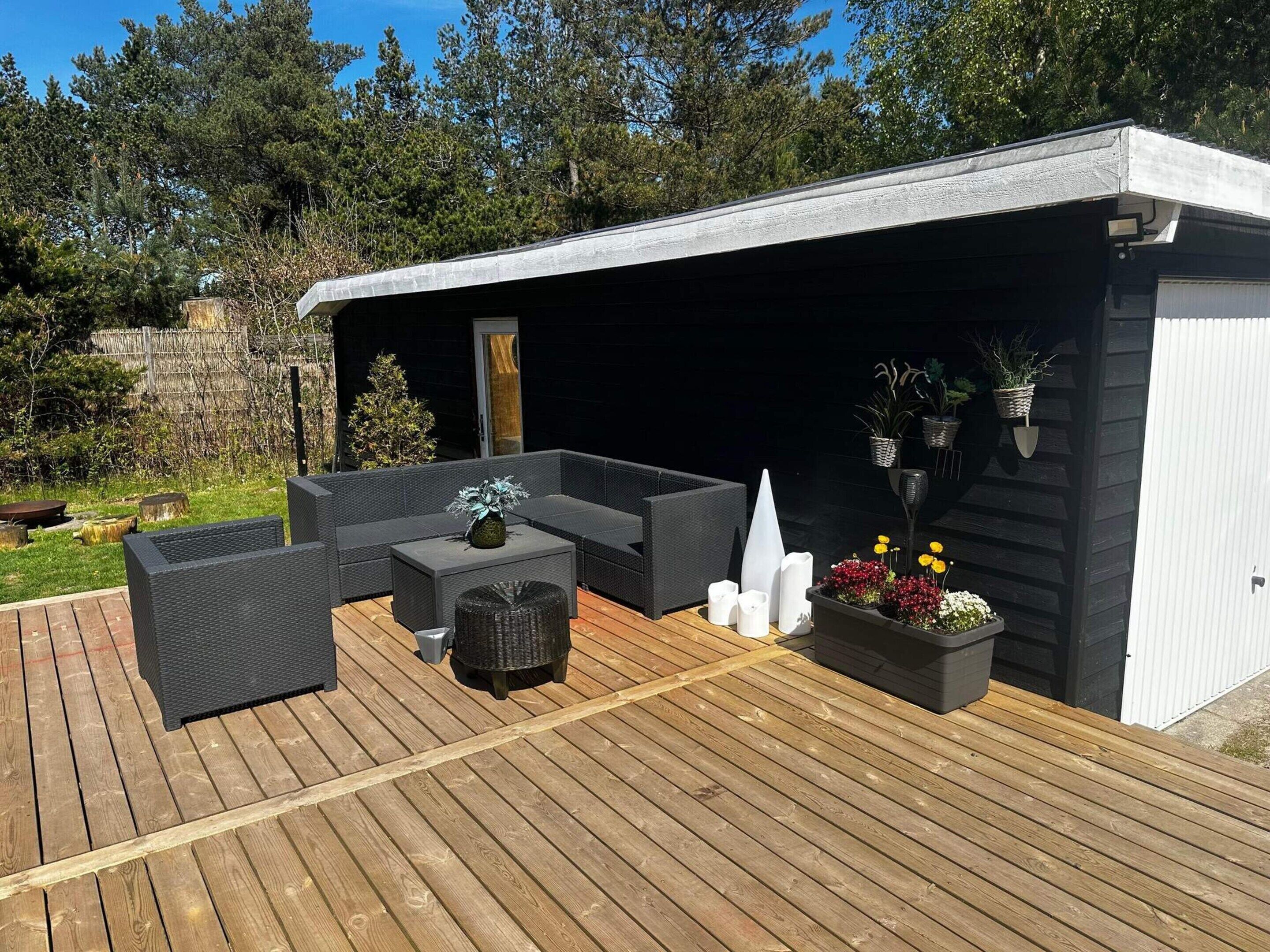 A covered outdoor seating area with a dark-colored sofa, a small table, and potted plants.