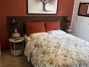 A bedroom with a bed, pillows, a bedside table, a lamp, and a framed artwork on the wall.