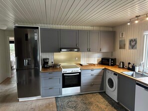 A modern kitchen with grey cabinets, a stainless steel refrigerator, a stove, a microwave, and a washing machine. - 4 Star Holiday Home in Hovborg (Hovborg)