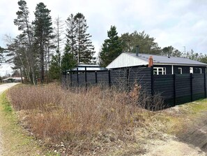 A small, dark wooden structure with a metal roof, surrounded by tall trees and dry vegetation. - 4 Star Holiday Home in Hovborg (Hovborg)