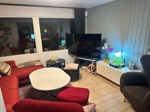 A living room with a TV, red sofas, a white table, and a fish tank.