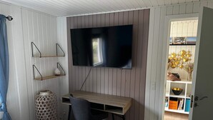 Un dormitorio con cama, un escritorio y silla, un televisor en la pared y una puerta que da a un baño.