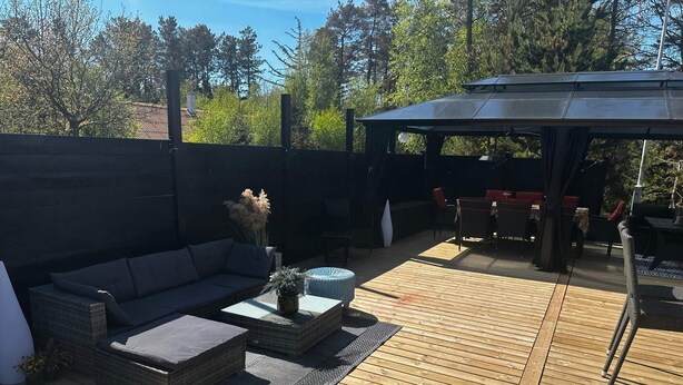 Terraza al aire libre con sofá, reposapiés y un  área de estar techada.