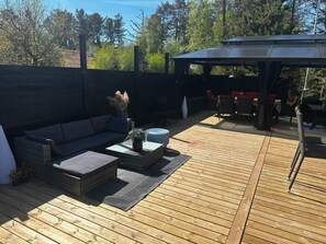 An outdoor deck with a sofa, ottoman, and a covered seating area. - 4 Star Holiday Home in Hovborg (Hovborg)