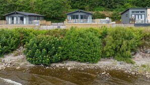 Une rangée de cabanes, avec une rivière au premier plan et des collines boisées en arrière-plan.