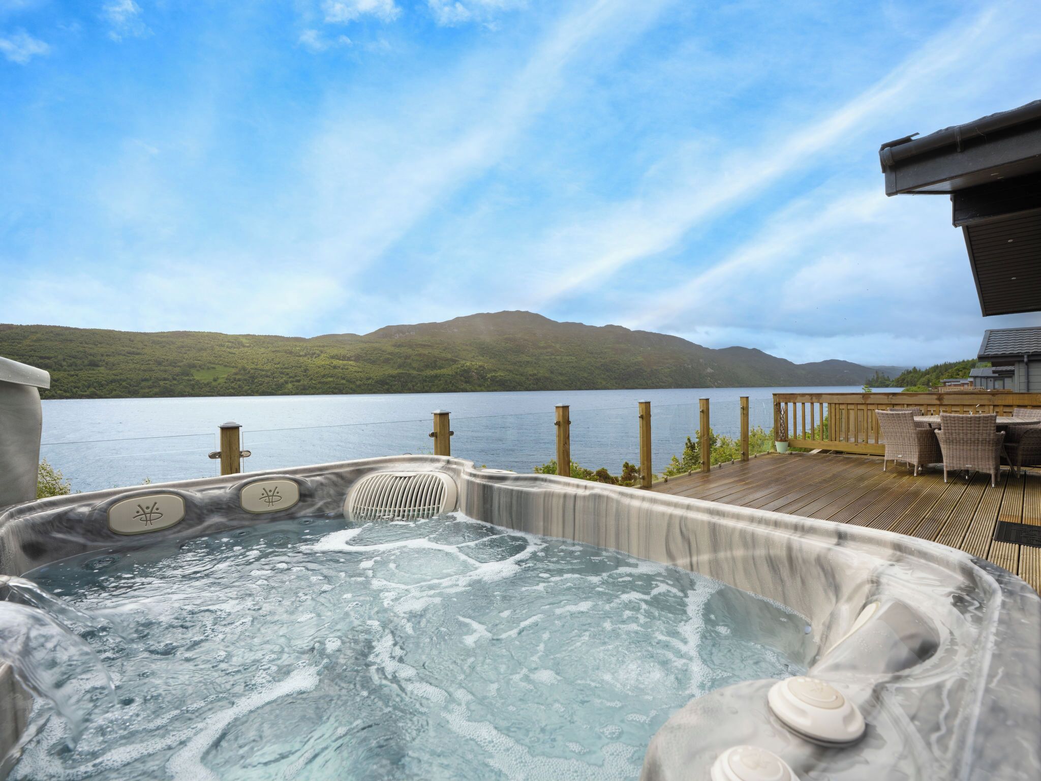A hot tub with a wooden deck and a view of a lake and mountains.