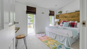 Une chambre à coucher avec un lit, une tête de lit en bois, une fenêtre, une porte et un petit tabouret.
