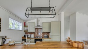 Une cuisine moderne avec un plan de travail en bois, des appareils électroménagers en acier inoxydable et un luminaire suspendu.