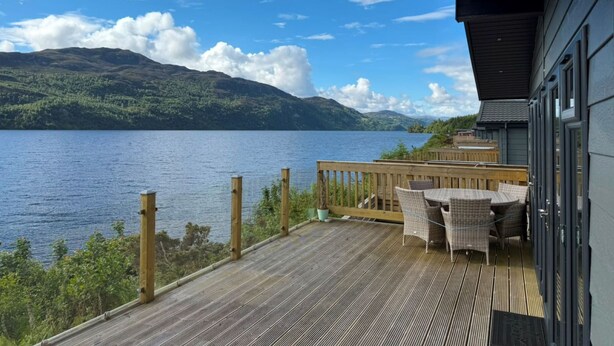Une terrasse en bois, agréée de mobilier d’extérieur, qui offre une vue sur un lac et des montagnes.