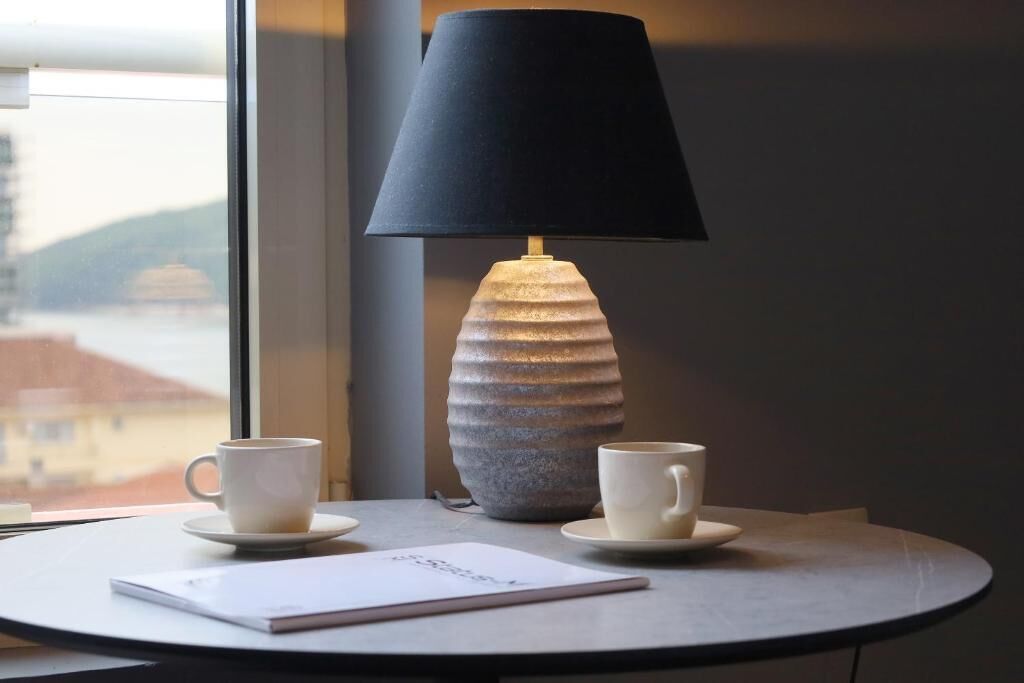 Et bord med to kopper og en lampe, et vindue med udsigt, og et stykke papir på bordet.