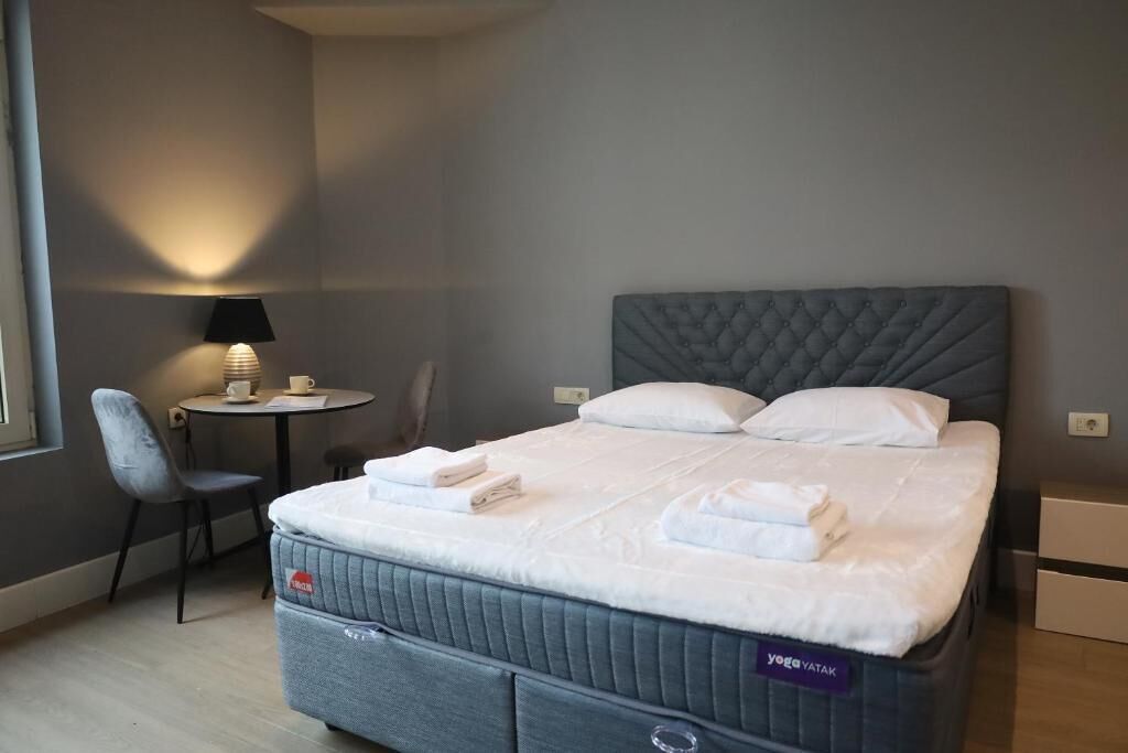 A hotel room with a bed, a small table with a lamp, a chair, and a desk.