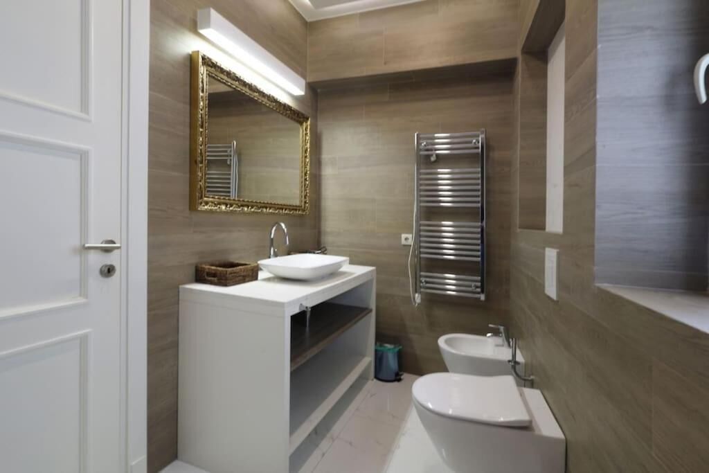 A modern bathroom with a white sink, a large mirror, a towel rack, and a bidet.