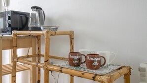 Una cadira de bambú amb encabonat al respatller i un taulell amb estovell amb dibuixos. Dues tasses marrons amb el text 'Felicidad Café' damunt el taulell.