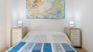 Un dormitori amb un llit, dues taules de nit, una petita taula i un quadre abstracte penjat a la paret, a més d'una finestra.