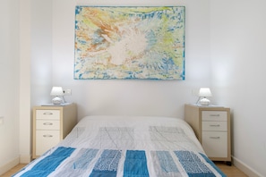 A bedroom with a bed, two bedside tables, a nightstand, a wall-mounted abstract painting, and a window. - Central Polynesia Apartment in Ronda (Ronda)