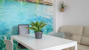 Habitació amb taula blanca, una planta en test, un sofà i un mural d'una platja tropical.