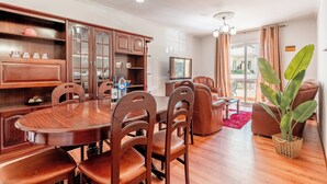 Uma sala de jantar com uma mesa e cadeiras de madeira, um armário com portas de vidro e uma planta grande.
