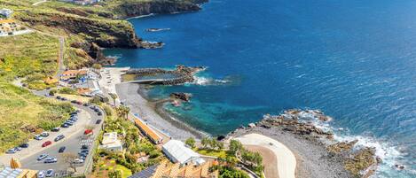 A coastal hotel with a parking lot, a beach, and rocky cliffs.