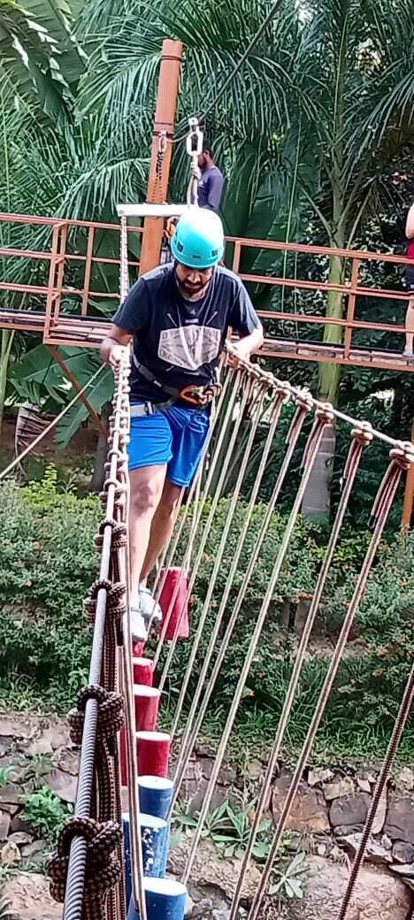 Une personne qui traverse un pont de corde dans un environnement extérieur, entourée de verdure.