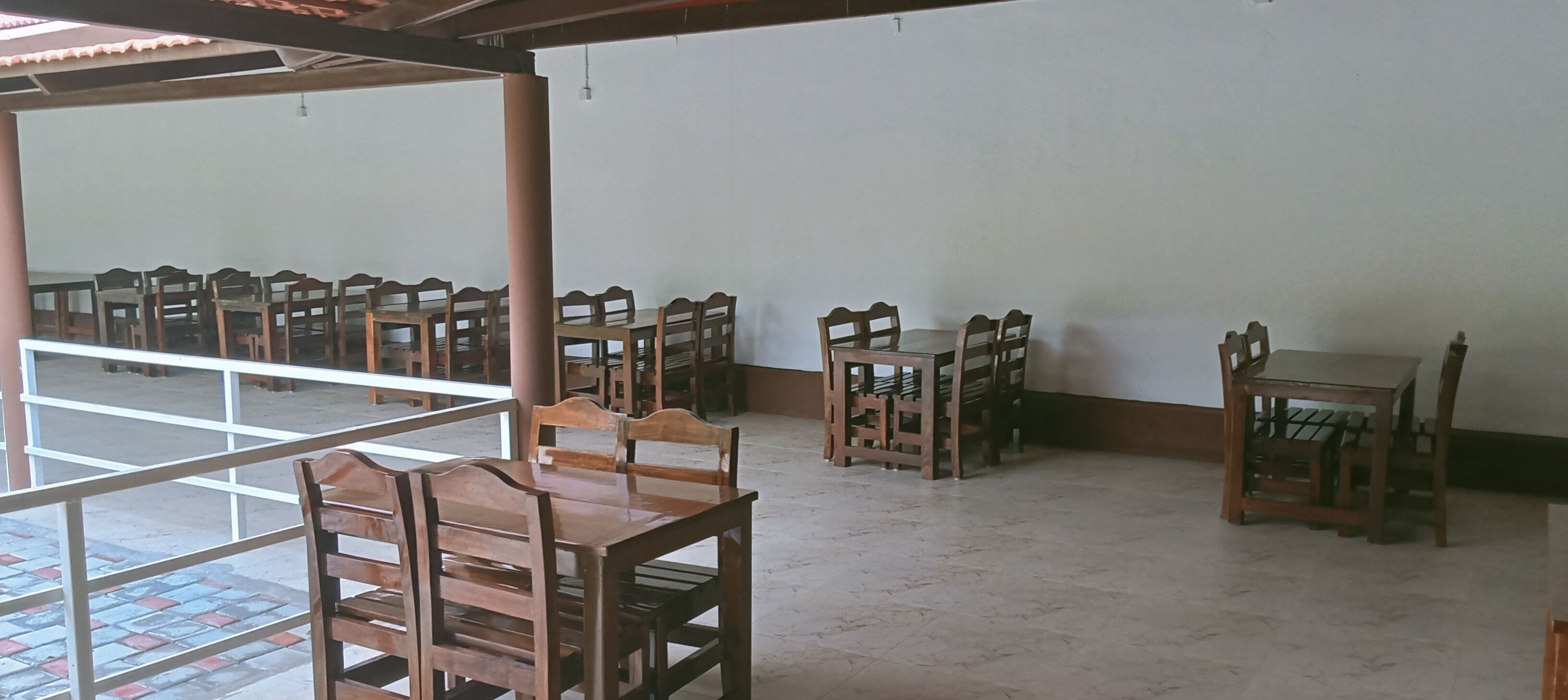 A room with multiple wooden tables and chairs arranged in rows, a tiled floor, and a white wall.