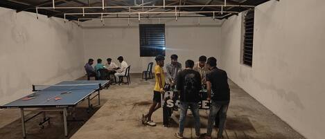 A room with a ping pong table, chairs, and a group of people.
