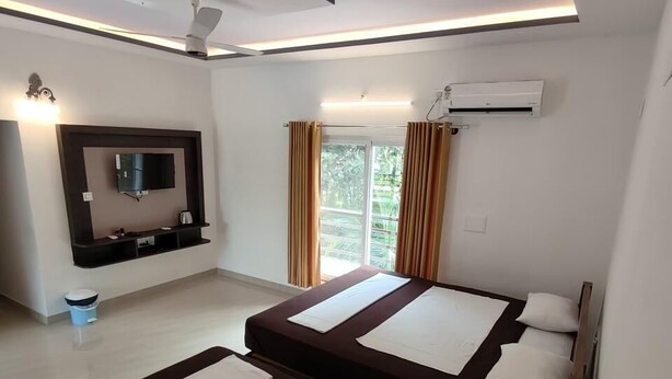 Habitación de hotel moderna con televisor de pantalla plana, ventilador de techo, cama grande con ropa de cama blanca y negra, y ventana con cortinas.