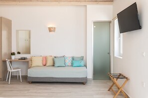Una habitación con sofá, escritorio, silla, televisor montado en la pared y una puerta.