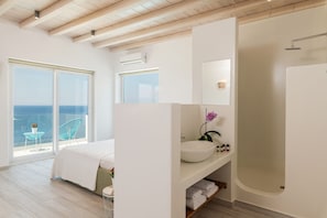 Un dormitorio moderno con un ventanal grande, una cama, un baño con bañera y un balcón con una silla.