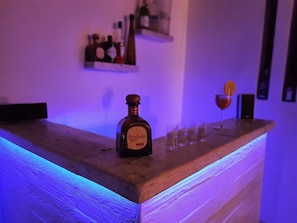 Uma área de bar com uma garrafa de tequila Don Julio, copos e uma garrafa de vinho sobre um balcão de madeira.